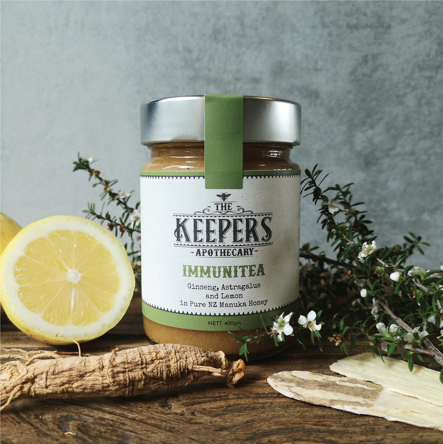 Jar of Immunitea blend with ginseng root and dried astragalus in the foreground, fresh lemon on the left and manuka branch on the right.